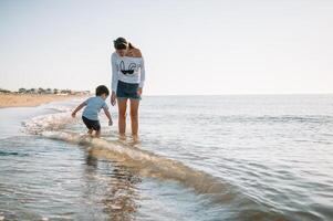 mãe e filho jogando em a de praia às a pôr do sol tempo. conceito do amigáveis família foto
