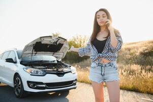 jovem sexy mulher com quebrado carro chamando em a célula telefone. foto