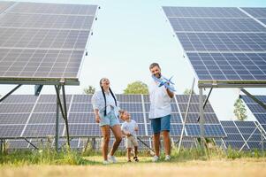 jovem família do três é agachado perto fotovoltaico solar painel, pequeno Garoto e pais. moderno família conceito. a conceito do verde energia foto