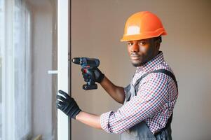 fechar-se do jovem africano faz-tudo dentro uniforme instalando janela foto