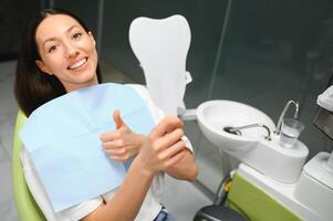 a menina sorrisos dentro odontologia. dentro a mãos do a espelho foto