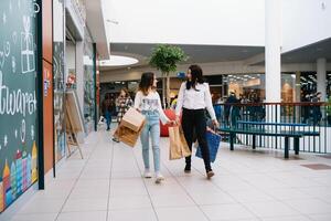 lindo jovem mãe e Adolescência filha estão segurando compras bolsas e sorridente enquanto fazendo compras dentro shopping center. família compras foto