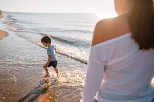 mãe e filho jogando em a de praia às a pôr do sol tempo. conceito do amigáveis família foto