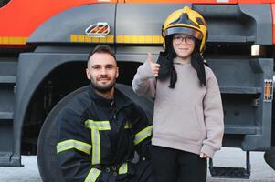 uma bombeiro mostra dele trabalhos para dele jovem filho. uma Garoto dentro uma de bombeiro capacete foto