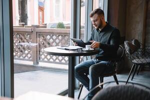 bonito homem de negocios usando uma digital tábua e bebendo café enquanto sentado dentro cafeteria dentro a cidade Centro. foto