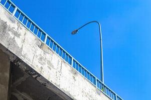 uma rua luminária em a lado do a estrada acima a mosca sobre ponte a partir de a ponto de vista do a mais baixo parte do a ponte contra uma brilhante azul céu fundo foto