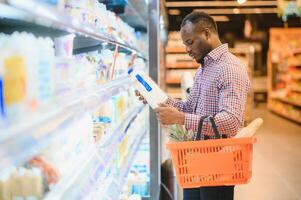 africano homem compras às supermercado. bonito cara segurando compras cesta foto