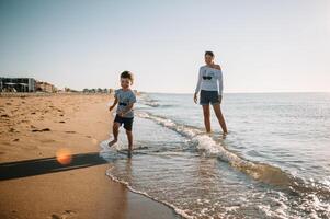 mãe e filho jogando em a de praia às a pôr do sol tempo. conceito do amigáveis família foto