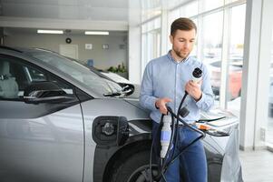 barba homem tentando uma Novo cobrando cabo com uma carro cobrando estação às a motor concessionária. conceito do comprando elétrico veículo. inteligente ecológico vivo foto