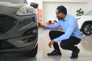 dele Sonhe carro. feliz jovem africano homem olhando animado escolhendo uma carro às a concessionária foto