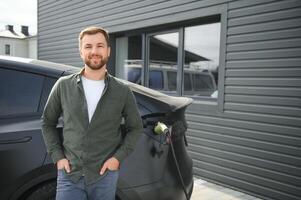 uma homem cobranças dele moderno elétrico carro. a conceito do verde energia foto