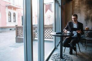 bonito homem de negocios usando uma digital tábua e bebendo café enquanto sentado dentro cafeteria dentro a cidade Centro. foto
