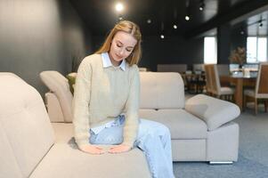 retrato do jovem alegre mulher teste sofá dentro mobília loja foto
