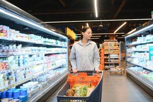 feliz jovem mulher olhando às produtos às mercearia loja. sorridente mulher compras dentro supermercado foto