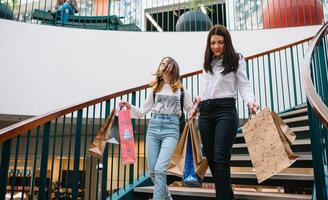 lindo jovem mãe e Adolescência filha estão segurando compras bolsas e sorridente enquanto fazendo compras dentro shopping center. família compras foto