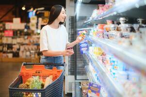 jovem sorridente feliz mulher 20s dentro casual roupas compras às supermercado loja com mercearia carrinho foto