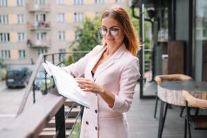 bem sucedido o negócio mulher com financeiro documentos em pé perto uma ampla janela dentro uma moderno escritório foto