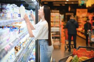 jovem sorridente feliz mulher 20s dentro casual roupas compras às supermercado loja com mercearia carrinho foto