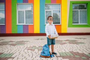 fofa estudante dentro branco camisas e uma óculos com livros e uma mochila. costas para escola. foto