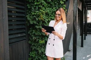 retrato do uma bem sucedido empresária segurando uma digital tábua almofada e uma pasta enquanto orgulhosamente em pé perto escritório. foto