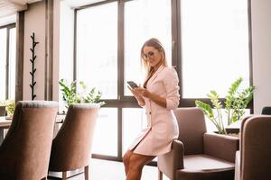 o negócio mulher em a telefone às escritório. jovem o negócio mulher tendo telefone ligar às a escritório. sorridente o negócio mulher. bonita jovem o negócio usando Smartphone às a loft escritório. foto