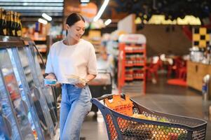 jovem satisfeito Diversão mulher dentro casual roupas compras às supermercado loja com mercearia carrinho foto