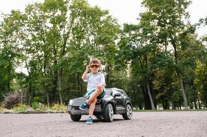 fofa Garoto dentro equitação uma Preto elétrico carro dentro a parque. engraçado Garoto passeios em uma brinquedo elétrico carro. cópia de espaço. foto