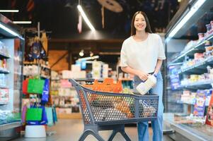 jovem sorridente feliz mulher 20s dentro casual roupas compras às supermercado loja com mercearia carrinho foto