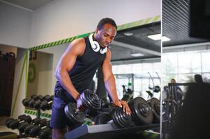 Preto masculino atleta levando haltere a partir de prateleira às Academia foto