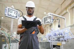 retrato do africano americano masculino engenheiro dentro uniforme e em pé dentro industrial fábrica foto