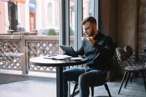 bonito homem de negocios usando uma digital tábua e bebendo café enquanto sentado dentro cafeteria dentro a cidade Centro. foto