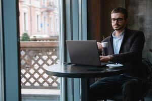 jovem bem sucedido homem de negocios trabalhando em uma computador portátil enquanto sentado dentro cafeteria foto