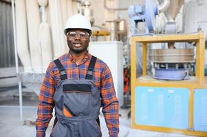 retrato do industrial engenheiro. sorridente fábrica trabalhador com Difícil chapéu em pé dentro fábrica Produção linha foto