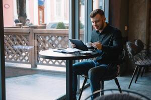 bonito homem de negocios usando uma digital tábua e bebendo café enquanto sentado dentro cafeteria dentro a cidade Centro. foto