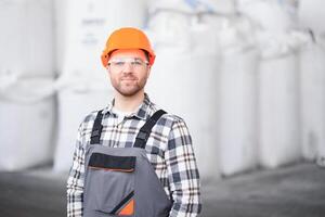 retrato do homem carregador dentro uniforme perto grande saco do café feijões ou trigo, nozes dentro armazém do fabricação fábrica foto