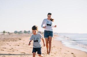 mãe e filho jogando em a de praia às a pôr do sol tempo. conceito do amigáveis família foto