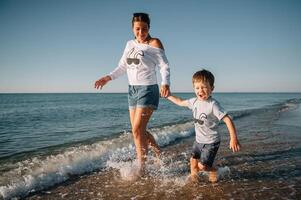 mãe e filho jogando em a de praia às a pôr do sol tempo. conceito do amigáveis família. foto
