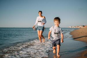 mãe e filho jogando em a de praia às a pôr do sol tempo. conceito do amigáveis família. foto