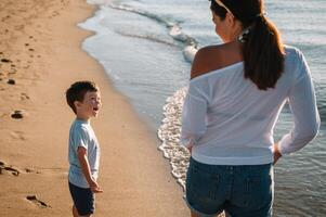 mãe e filho jogando em a de praia às a pôr do sol tempo. conceito do amigáveis família foto