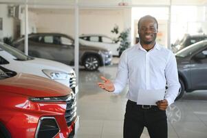 carros concessionária conceito. auto vendedor afro homem em pé dentro automóvel Centro foto