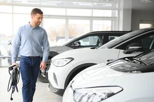 conceito do comprando elétrico veículo. bonito o negócio homem carrinhos perto elétrico carro às concessionária foto