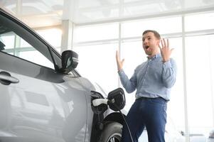 jovem homem, vendendo elétrico carros dentro a showroom. conceito do comprando ecológico carro para família foto