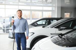 conceito do comprando elétrico veículo. bonito o negócio homem carrinhos perto elétrico carro às concessionária foto