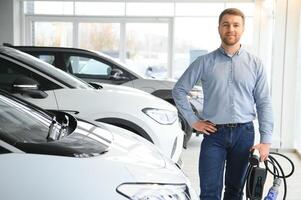 jovem homem, vendendo elétrico carros dentro a showroom. conceito do comprando ecológico carro para família foto