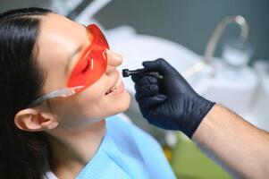 dentista cura a pacientes dentes com ultravioleta luminária dentro dele escritório foto