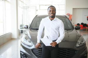 carros concessionária conceito. auto vendedor afro homem em pé dentro automóvel Centro foto