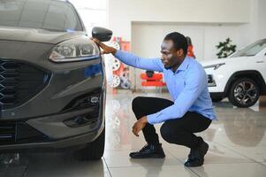 dele Sonhe carro. feliz jovem africano homem olhando animado escolhendo uma carro às a concessionária foto