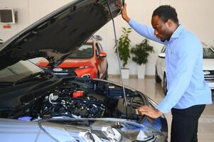 bonito africano homem de negocios é examinando uma carro antes comprando isto, ele Verificações todos características e características do auto foto