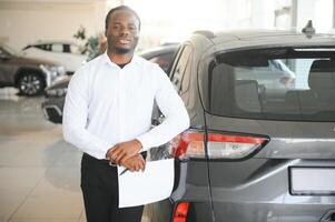 retrato do bonito africano americano vendedor às local de trabalho dentro carro sala de exposições foto