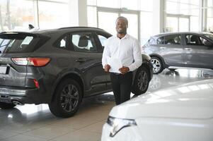 retrato do bonito africano americano vendedor às local de trabalho dentro carro sala de exposições foto